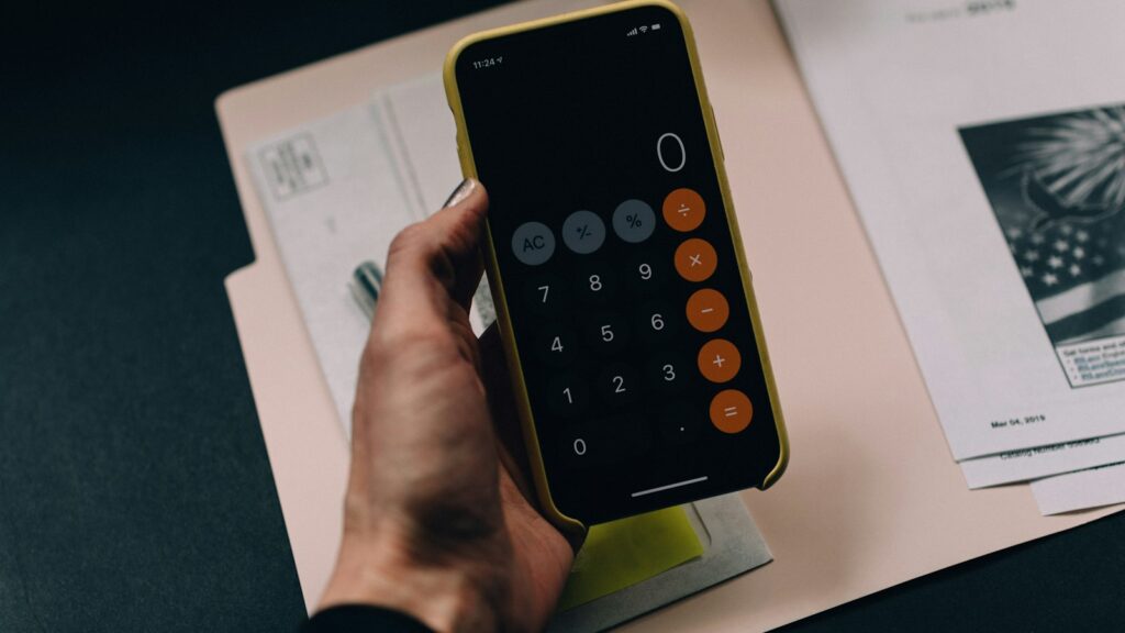 Hand holding a phone with a calculator app over paperwork
