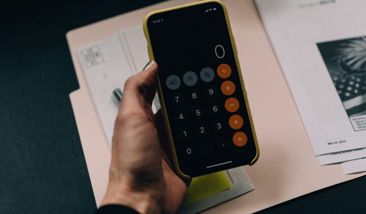 Hand holding a phone with a calculator app over paperwork